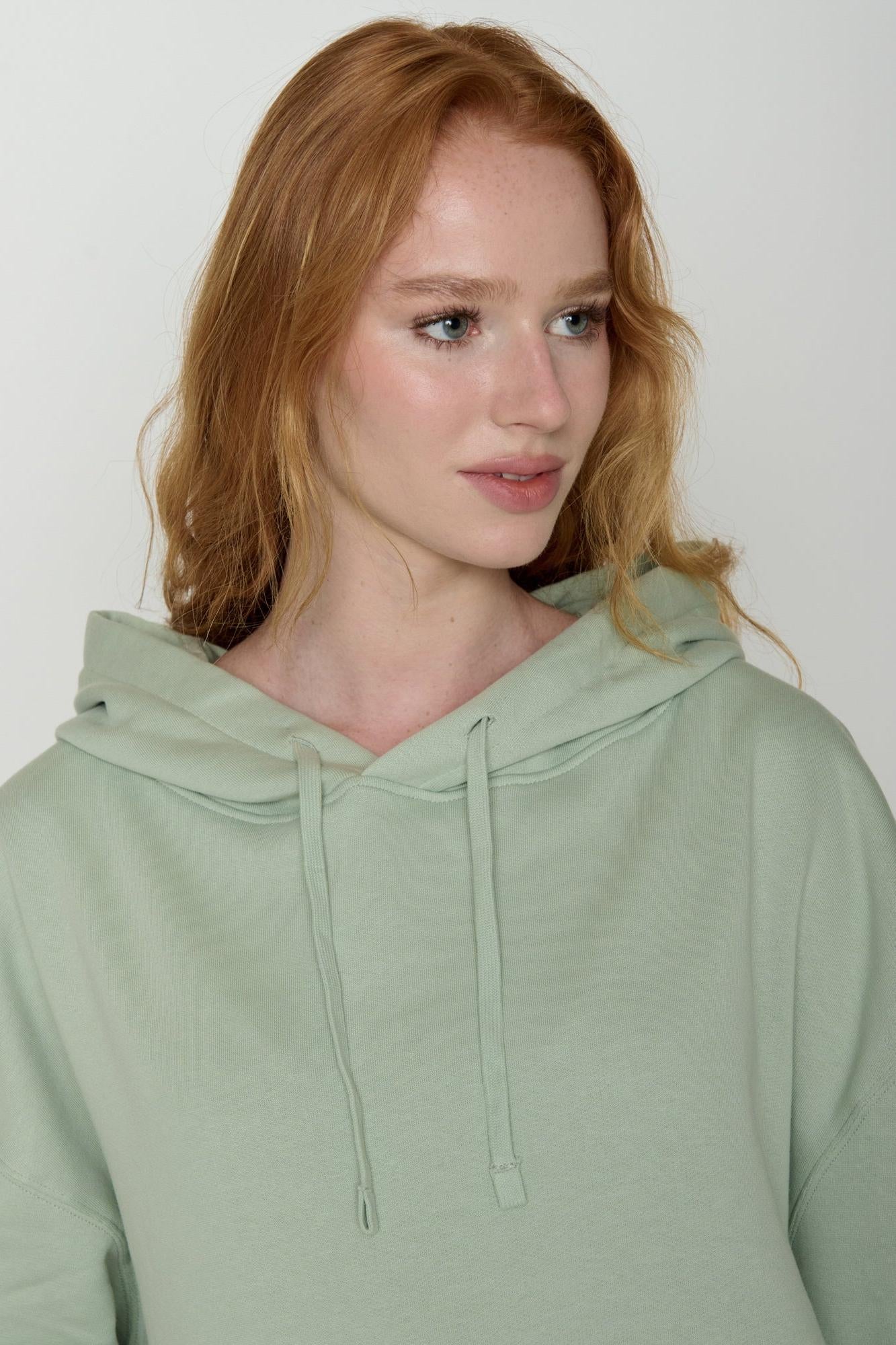 Woman wearing a light green organic cotton hoodie against a plain background