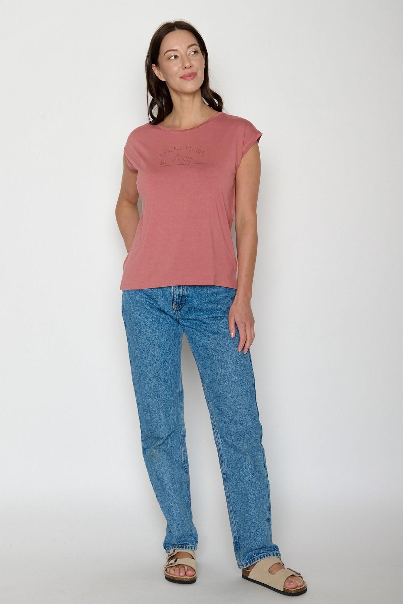 Woman wearing a pink Greenbomb t-shirt and blue jeans on a white background