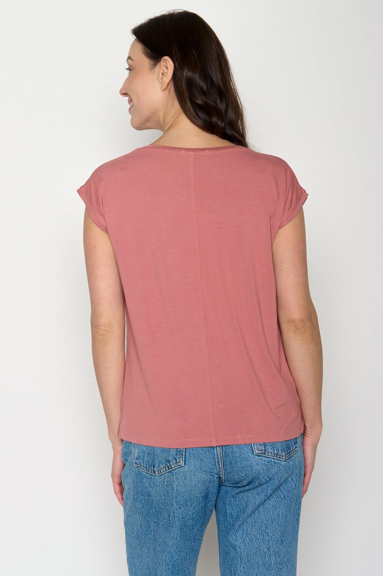 Woman wearing a pink eco-vero top and blue jeans against a white background