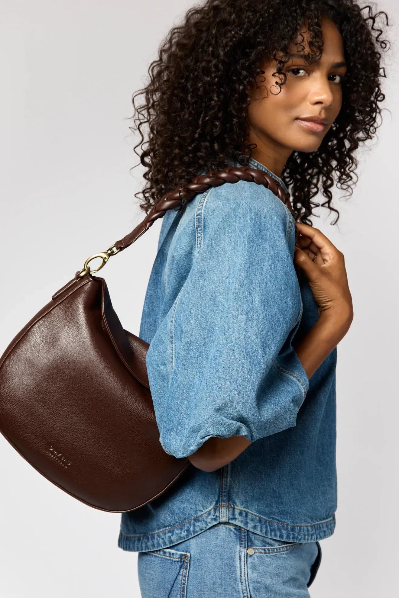 Woman wearing a brown leather handbag over her shoulder against a plain background