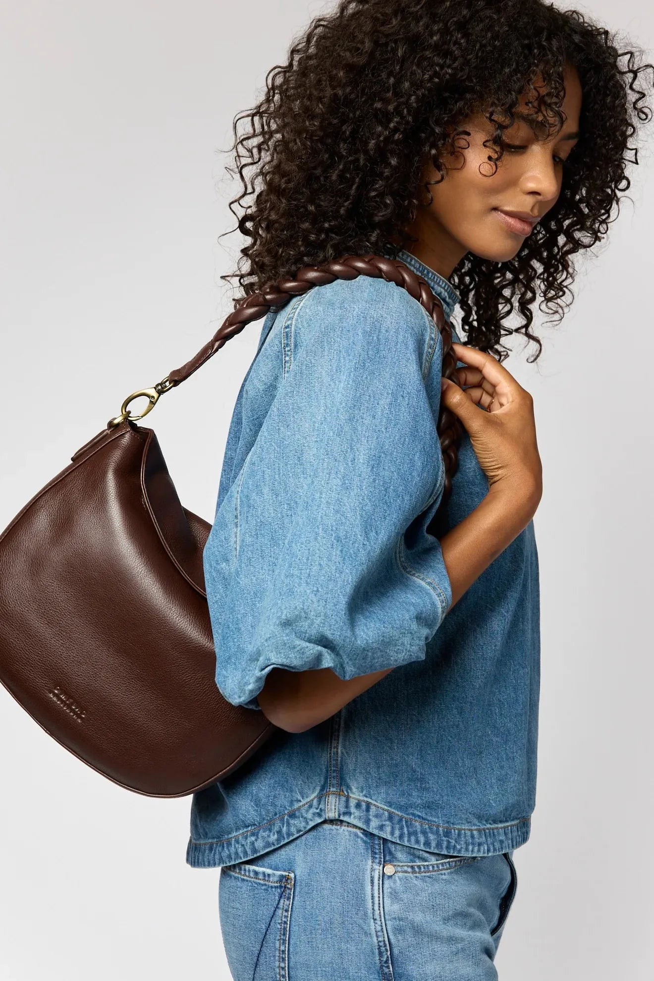 Woman holding a brown leather handbag against a plain background