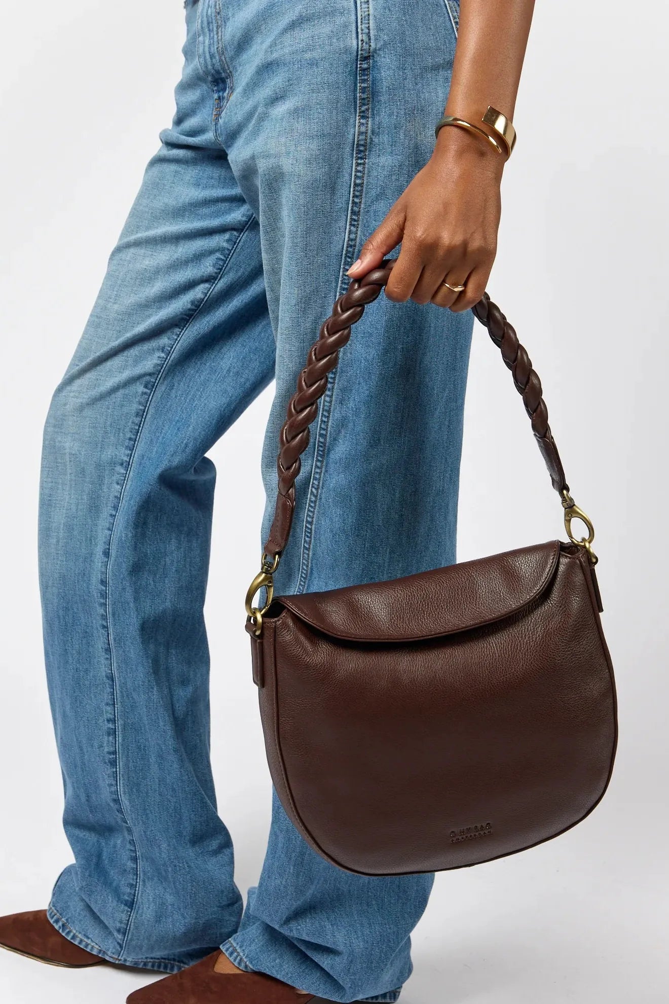 Brown leather handbag held by a person wearing blue jeans on a white background