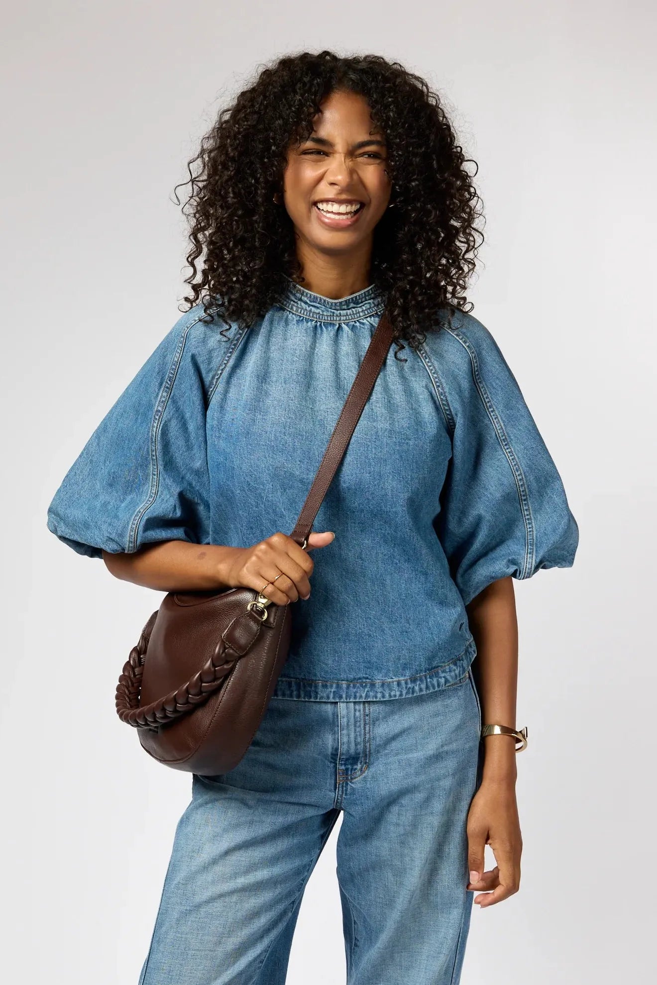 Woman wearing a denim outfit with a brown O My Bag leather bag on a plain background