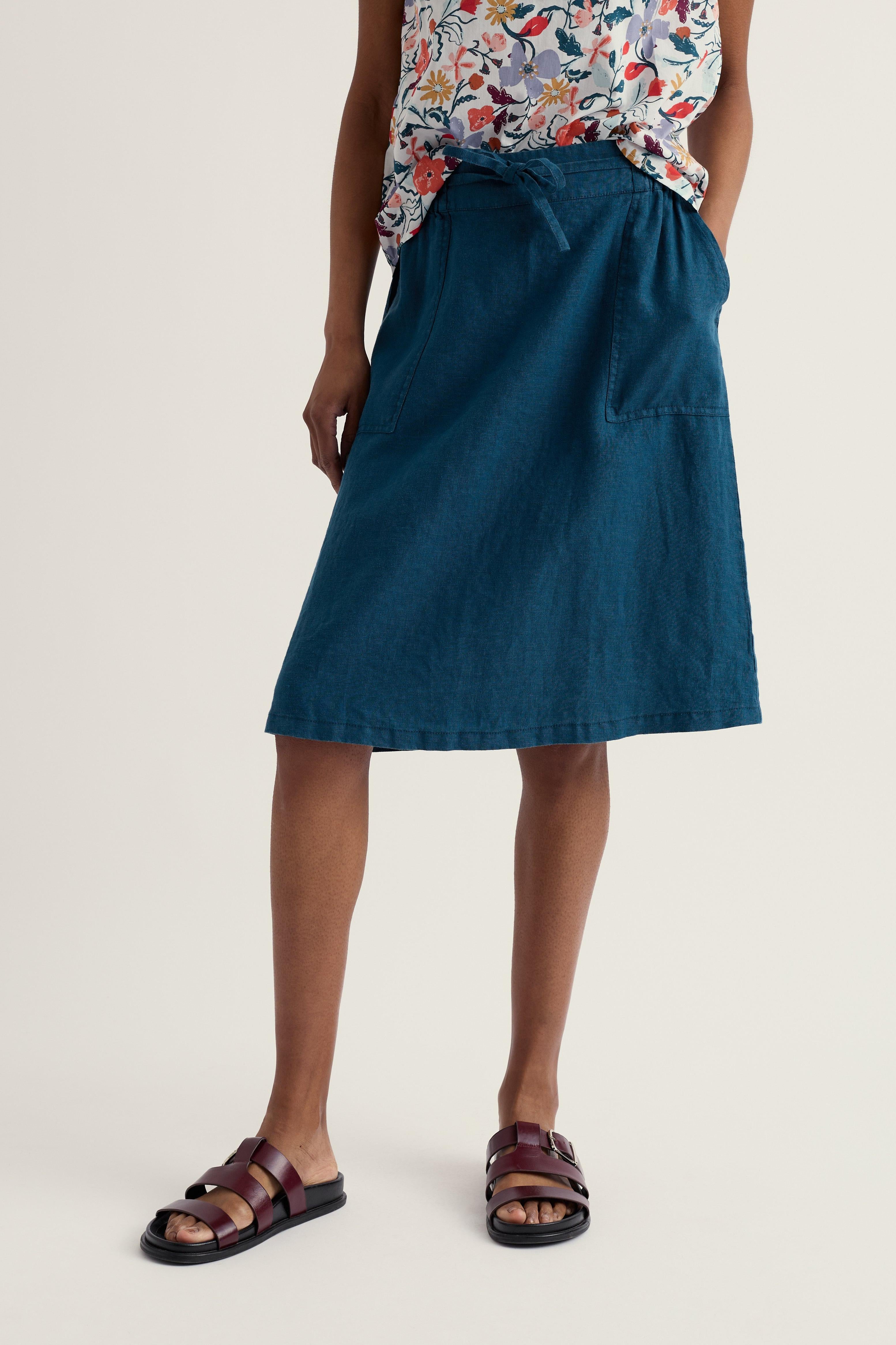 Person wearing a blue linen skirt and floral top on a beige background