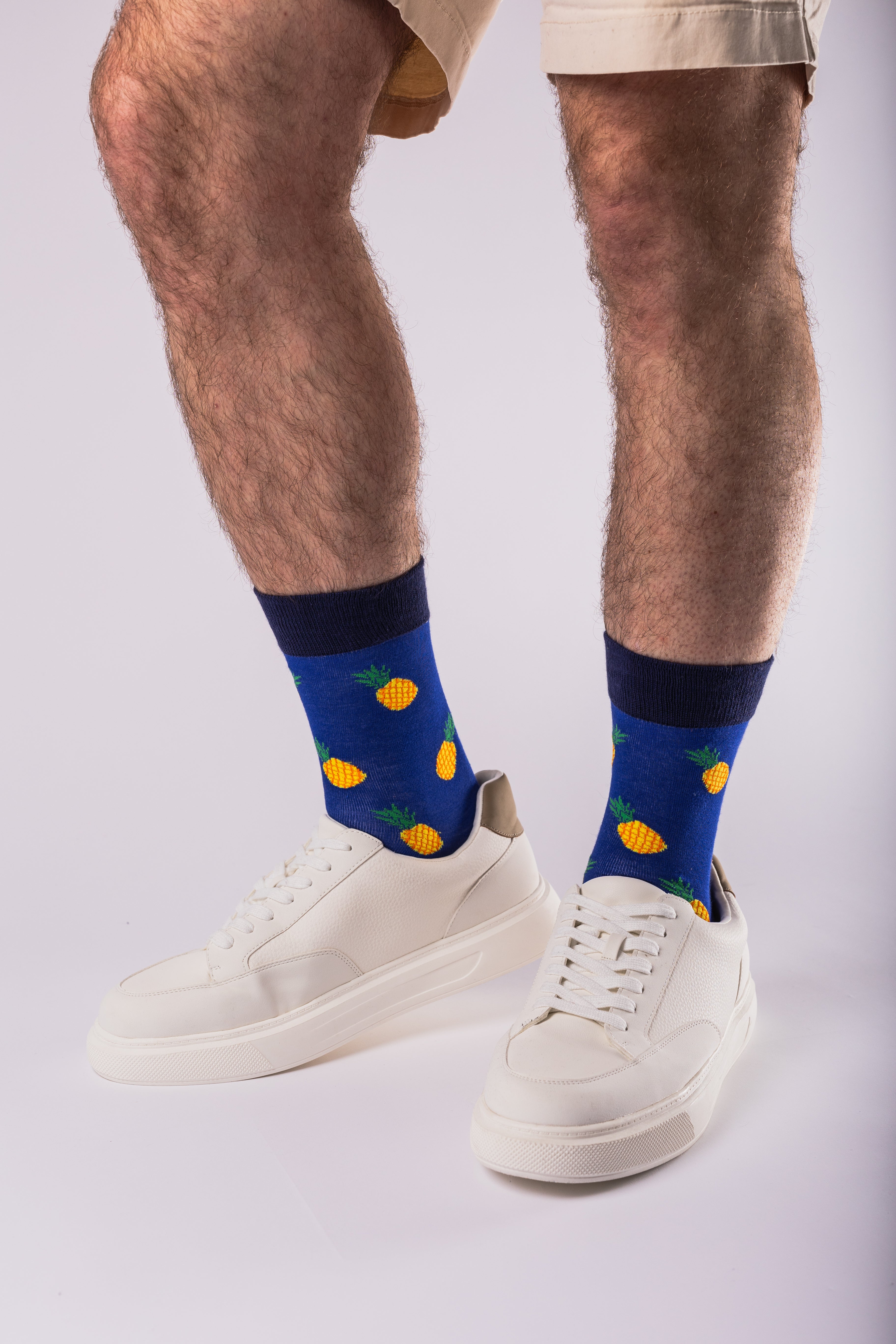 Person wearing blue socks with orange patterns and white sneakers on a light gray background