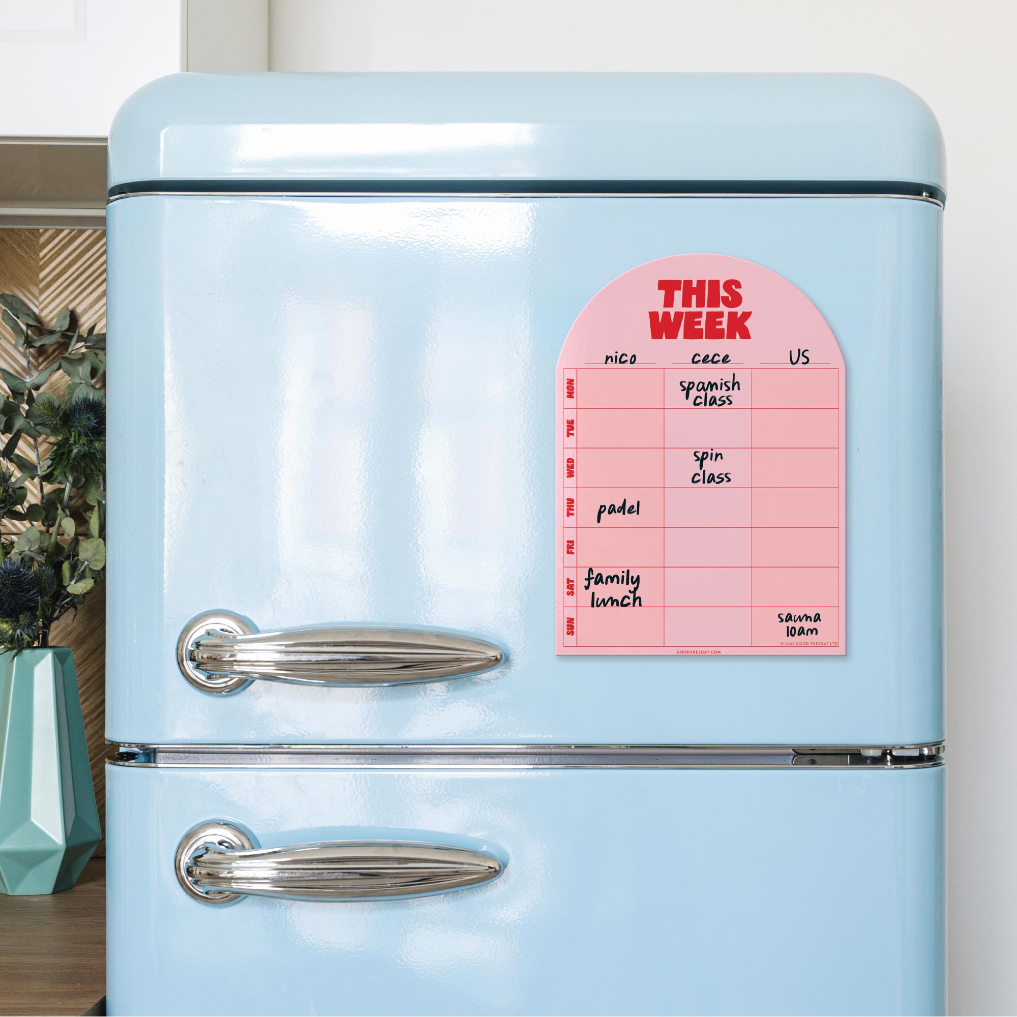 Light blue refrigerator with a pink magnetic notepad on a white wall.