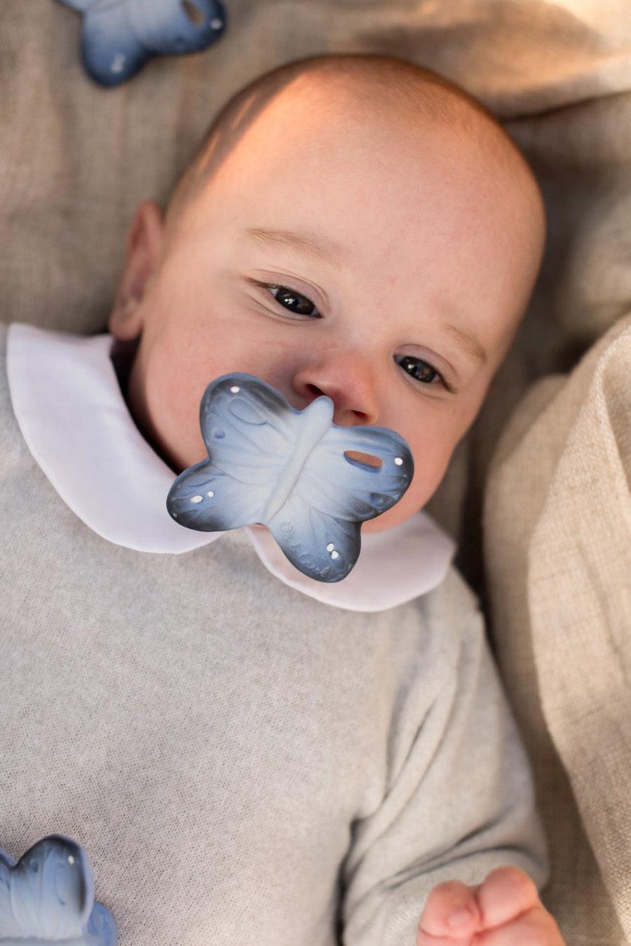 Baby wearing a butterfly-shaped natural rubber pacifier with a neutral background