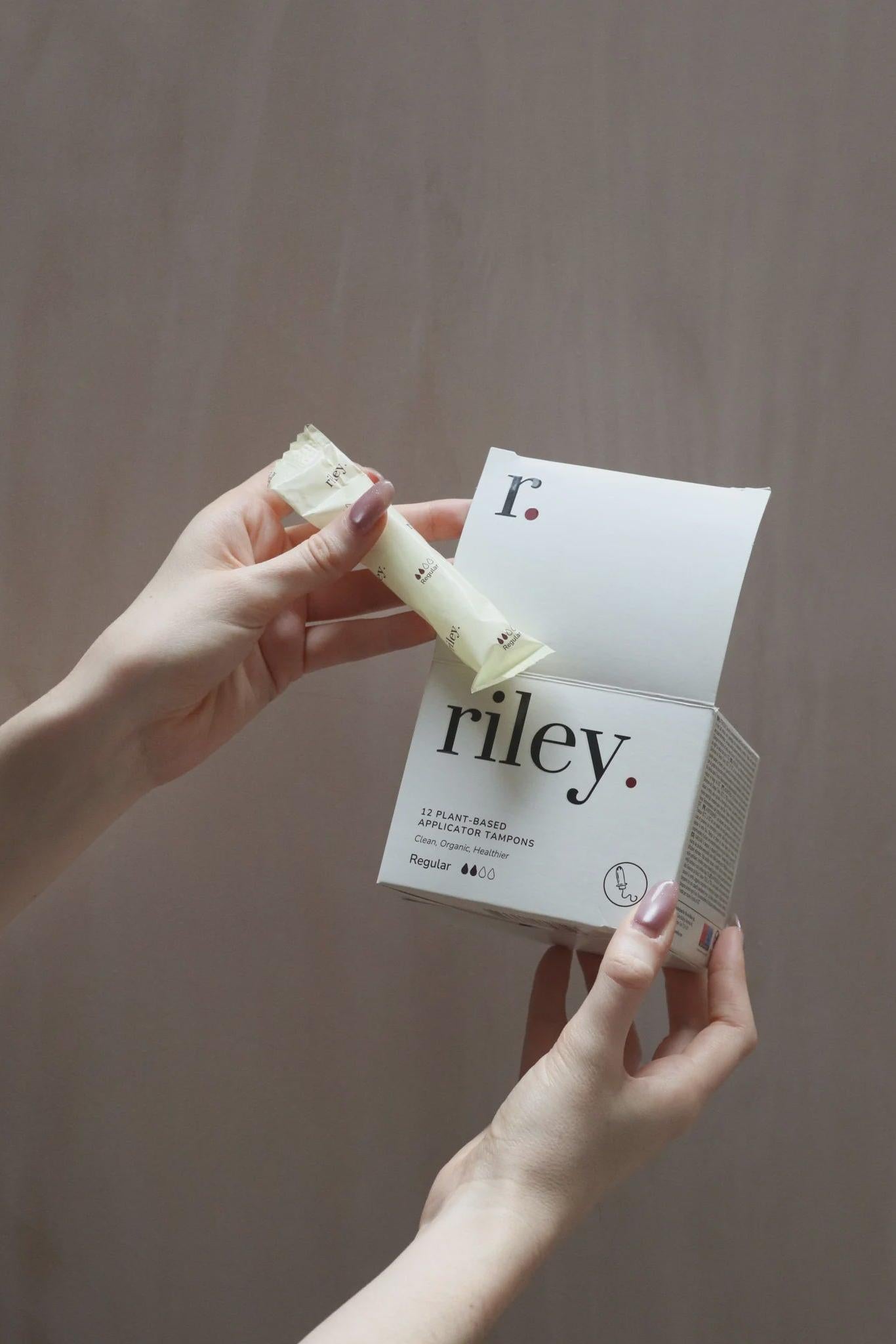 Hands holding a 'riley' organic cotton tampon and its packaging against a neutral background