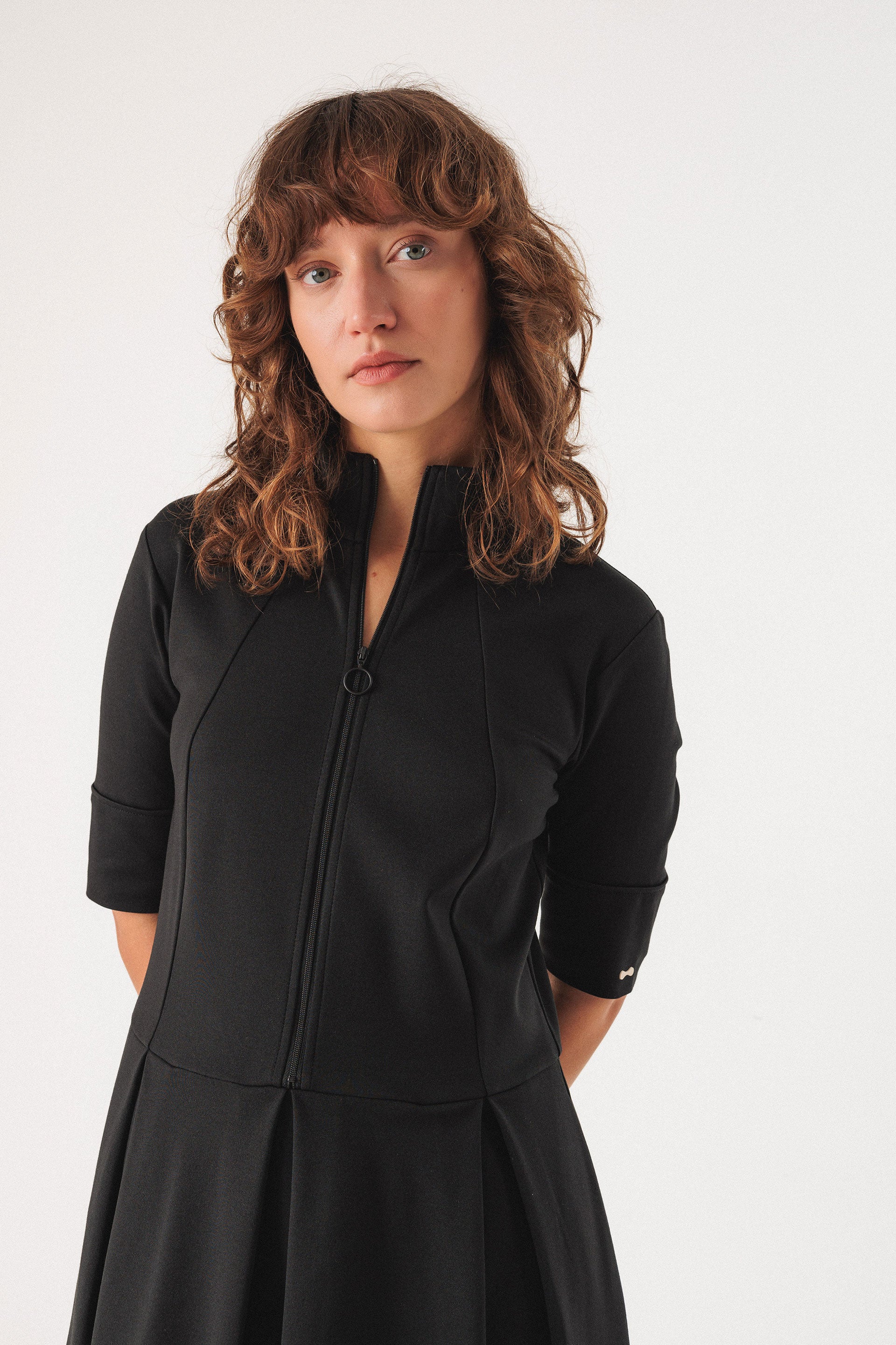 Woman wearing a black midi dress with a fitted bodice and gently flared skirt against a white background