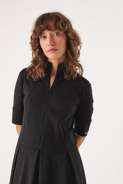 Woman wearing a black midi dress with a fitted bodice and gently flared skirt against a white background