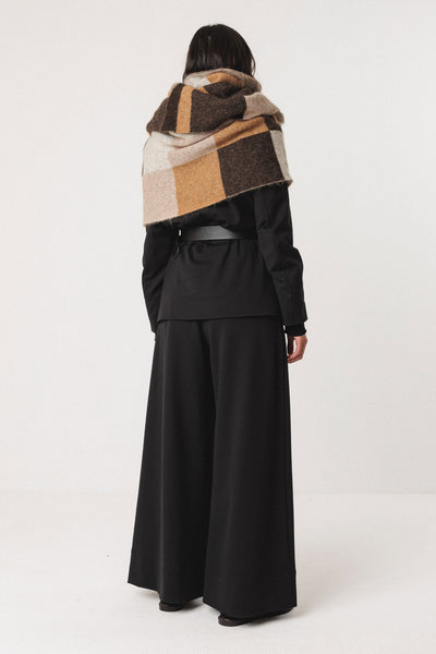 Person wearing a black outfit with a checkered wool scarf on a white background