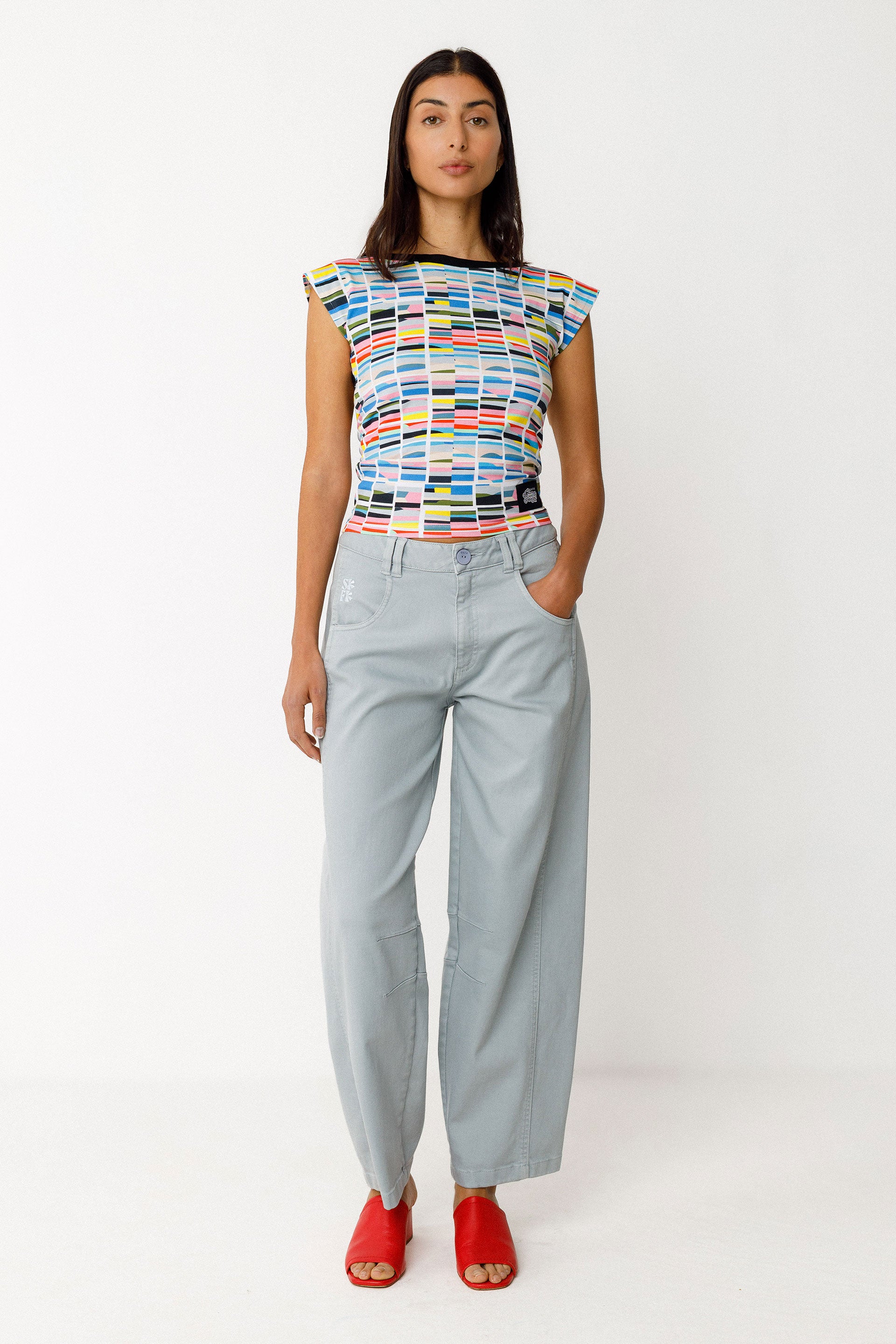 Woman wearing a colorful organic cotton top and light blue pants on a white background