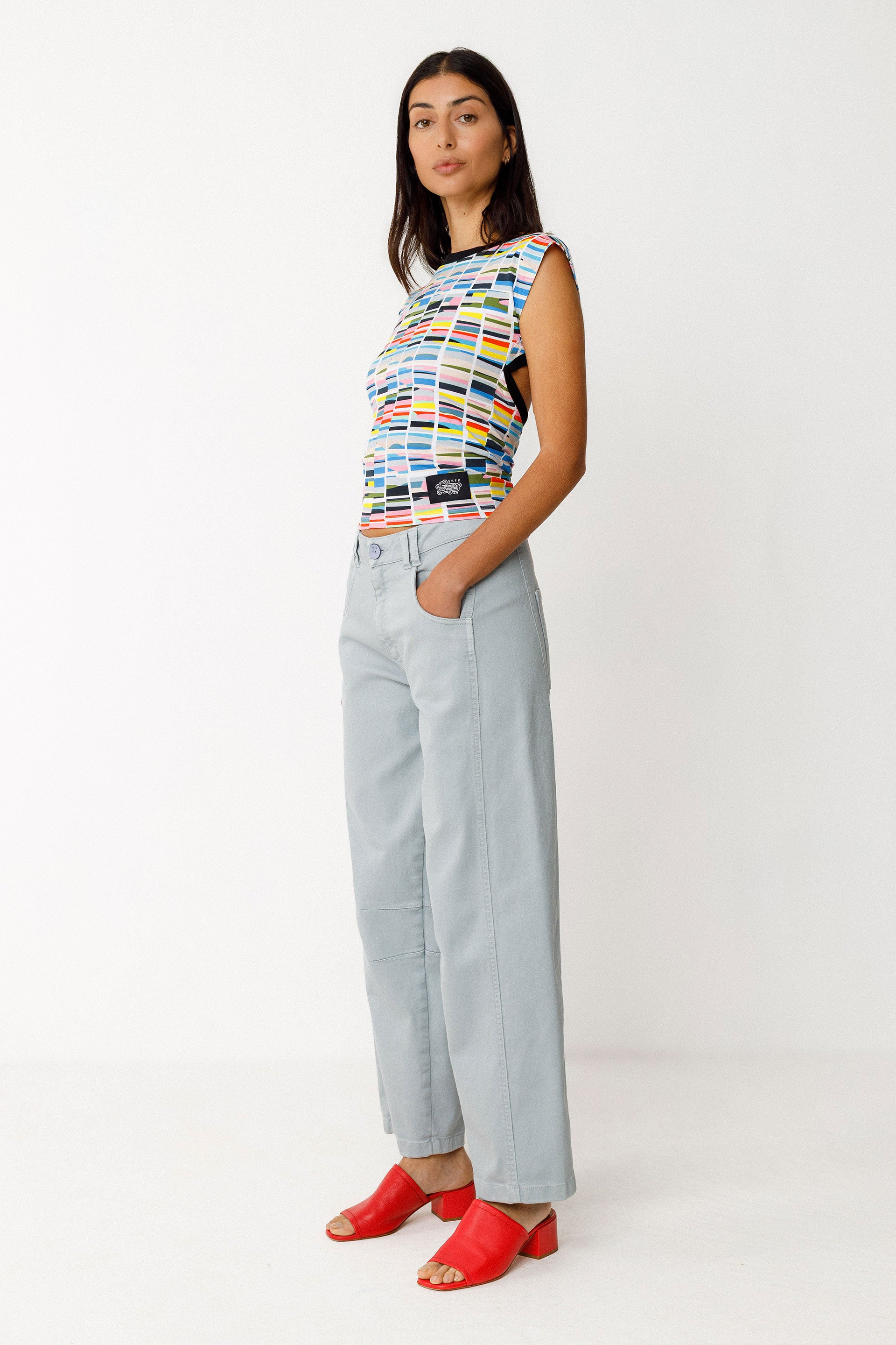 Woman wearing a colorful sleeveless top and light blue jeans on a white background