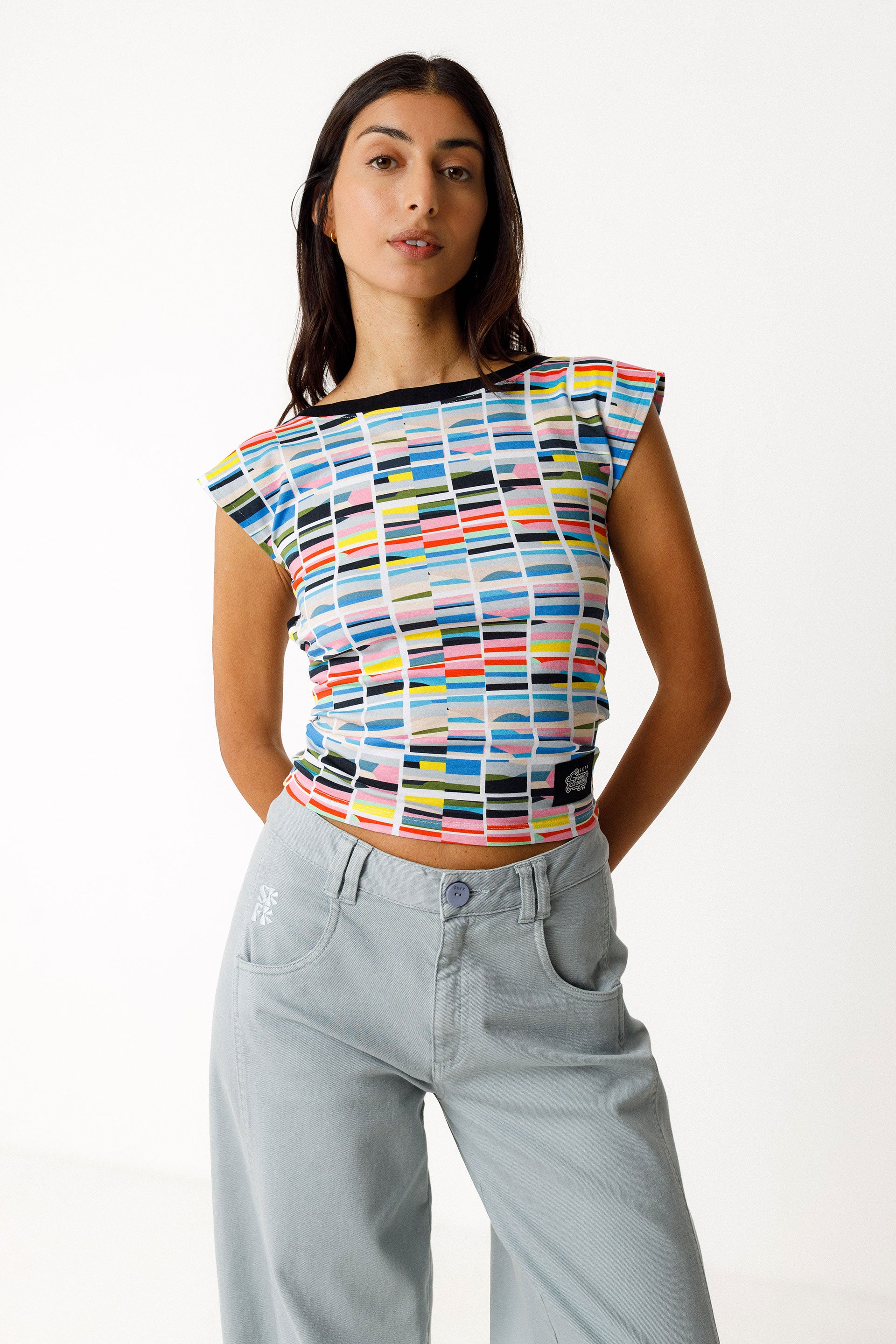 Woman wearing a colorful patterned top and light blue jeans on a white background