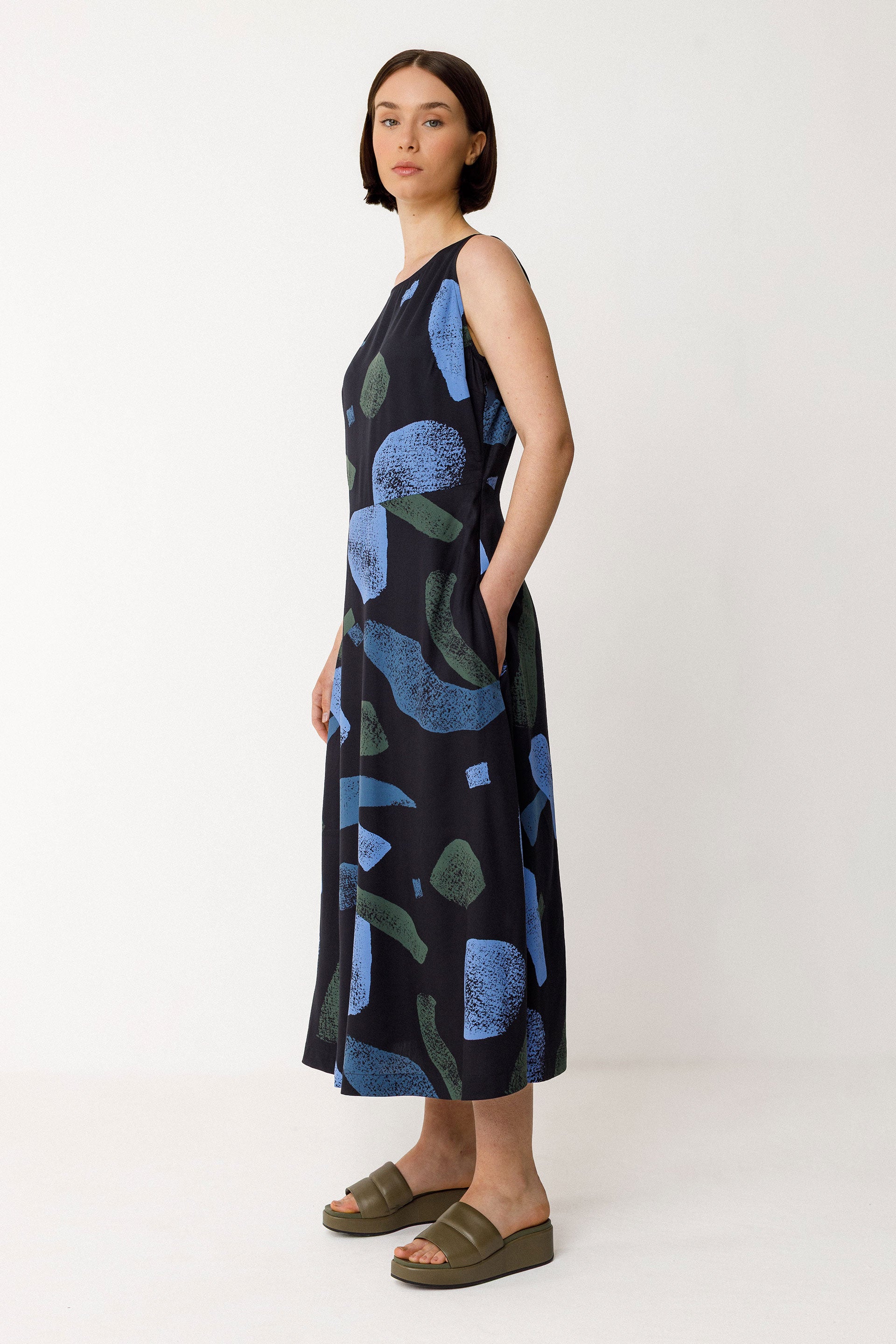 Woman wearing a black sleeveless dress with blue and green abstract patterns on a white background