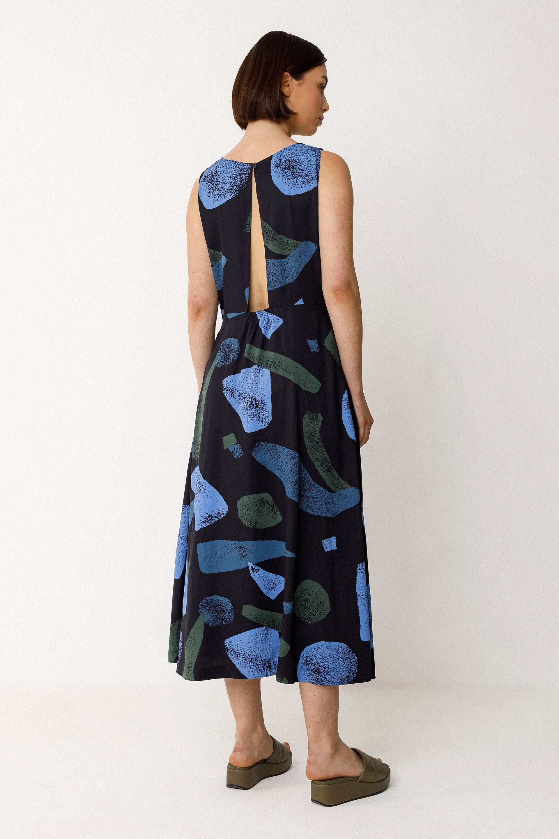 Woman wearing a black dress with blue abstract patterns and cut out back on a white background