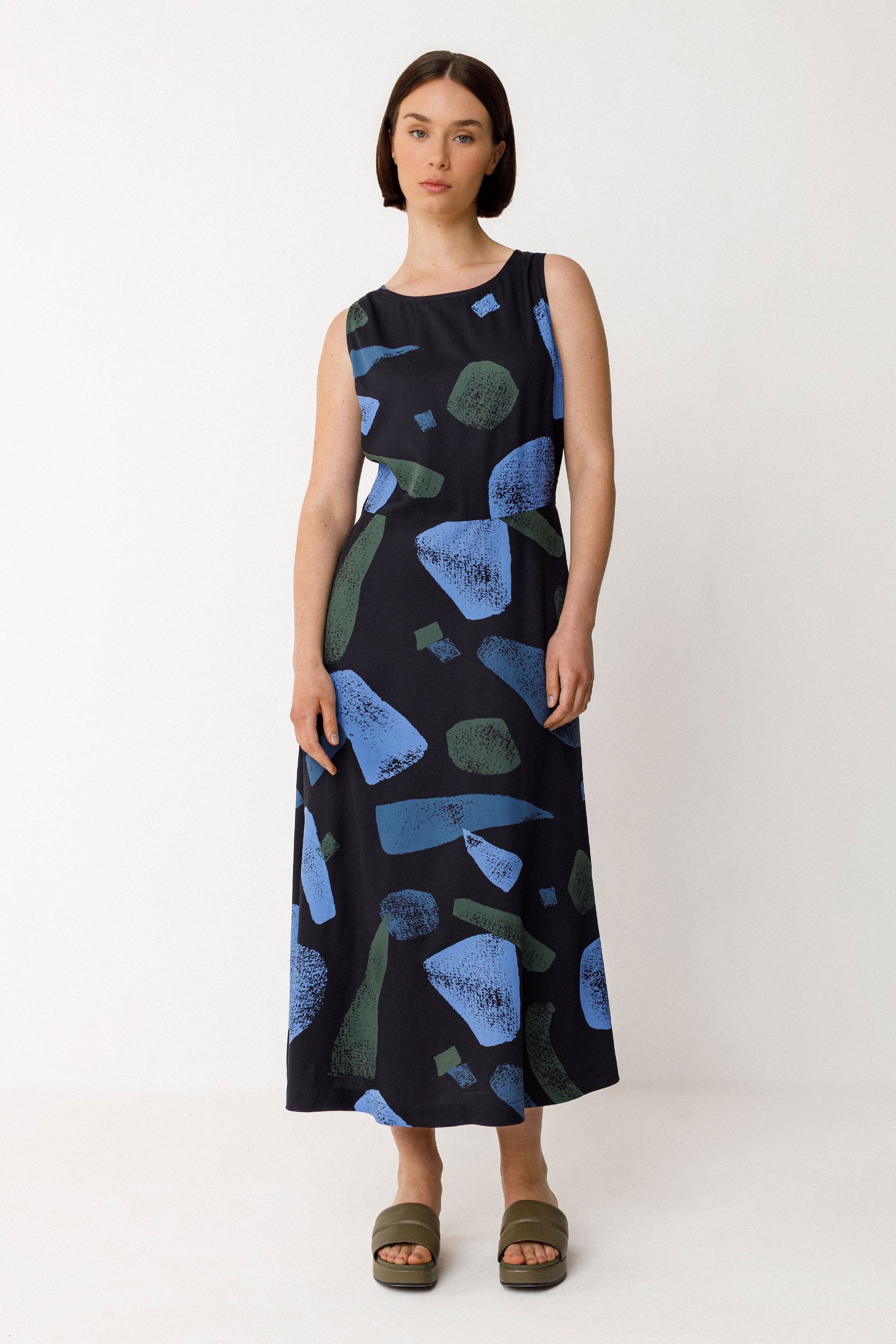 Woman wearing a sleeveless ecovero dress with abstract blue and green pattern on a white background