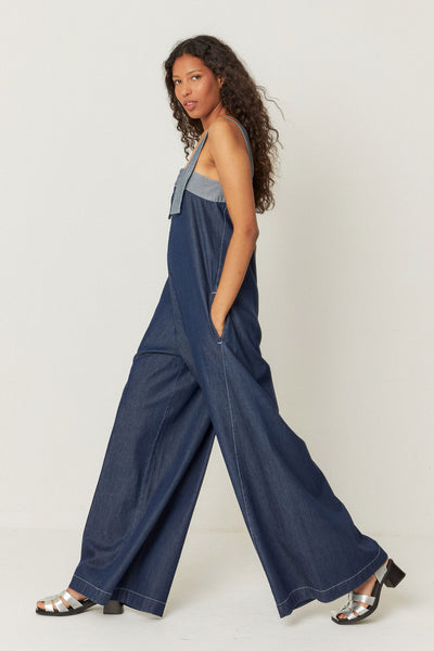 side view of model wearing long, relaxed-fit denim jumpsuit featuring front pockets, decorative stitching, and a zip closure