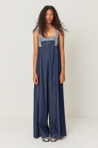 view of model wearing long, relaxed-fit denim jumpsuit featuring front pockets, decorative stitching, and a zip closure