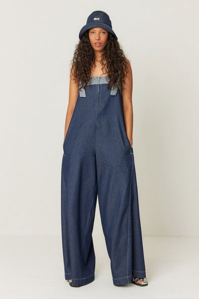 model wearing denim jumpsuit featuring front pockets, decorative stitching, and a zip closure