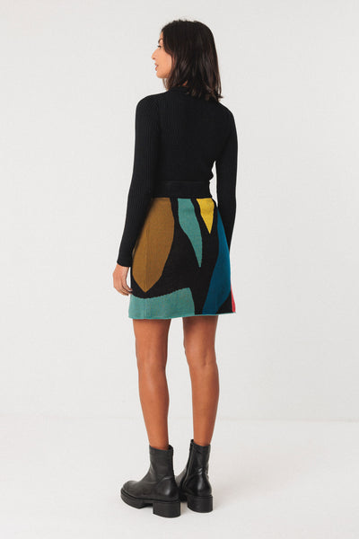Woman wearing patterned organic cotton skirt with black knit top and black boots on white background