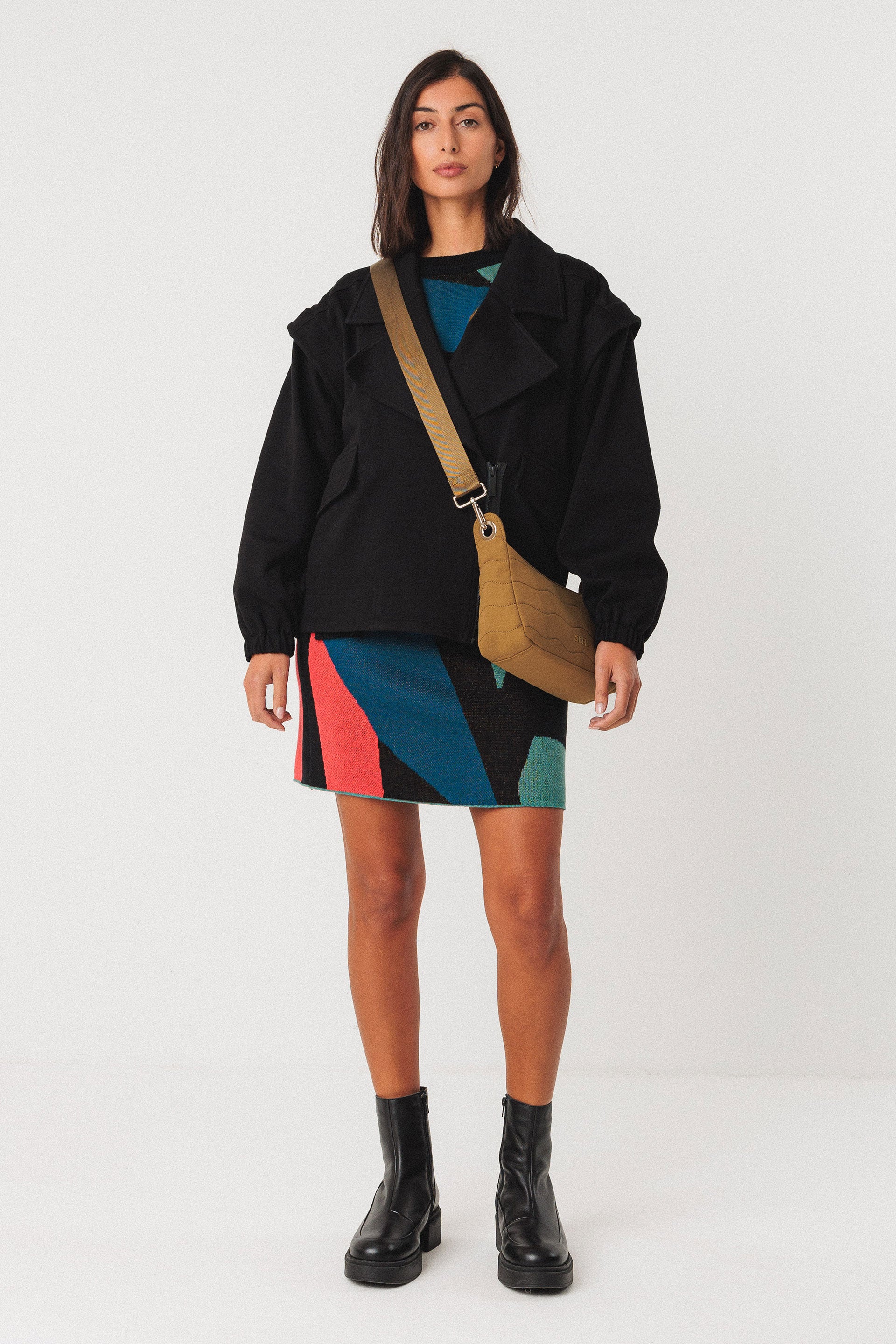Woman wearing a black jacket, colorful organic cotton knit skirt, and black boots on a white background