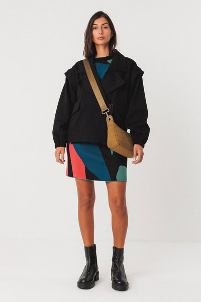 Woman wearing a black jacket, colorful organic cotton knit skirt, and black boots on a white background