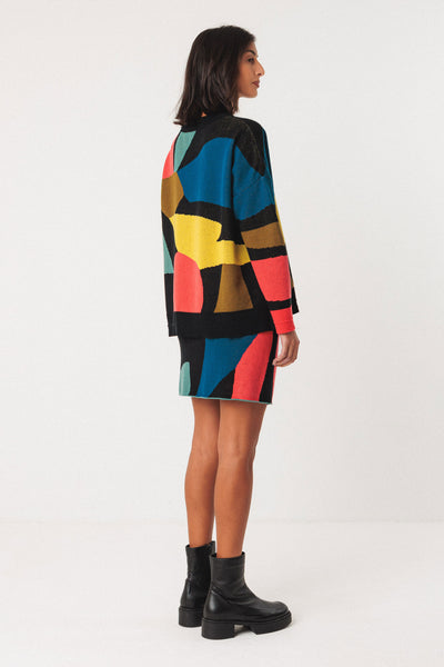 Person wearing a colourful organic cotton sweater and black boots on a white background
