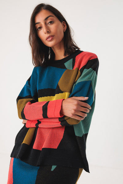 Woman wearing a colourful organic cotton sweater with geometric pattern on a white background