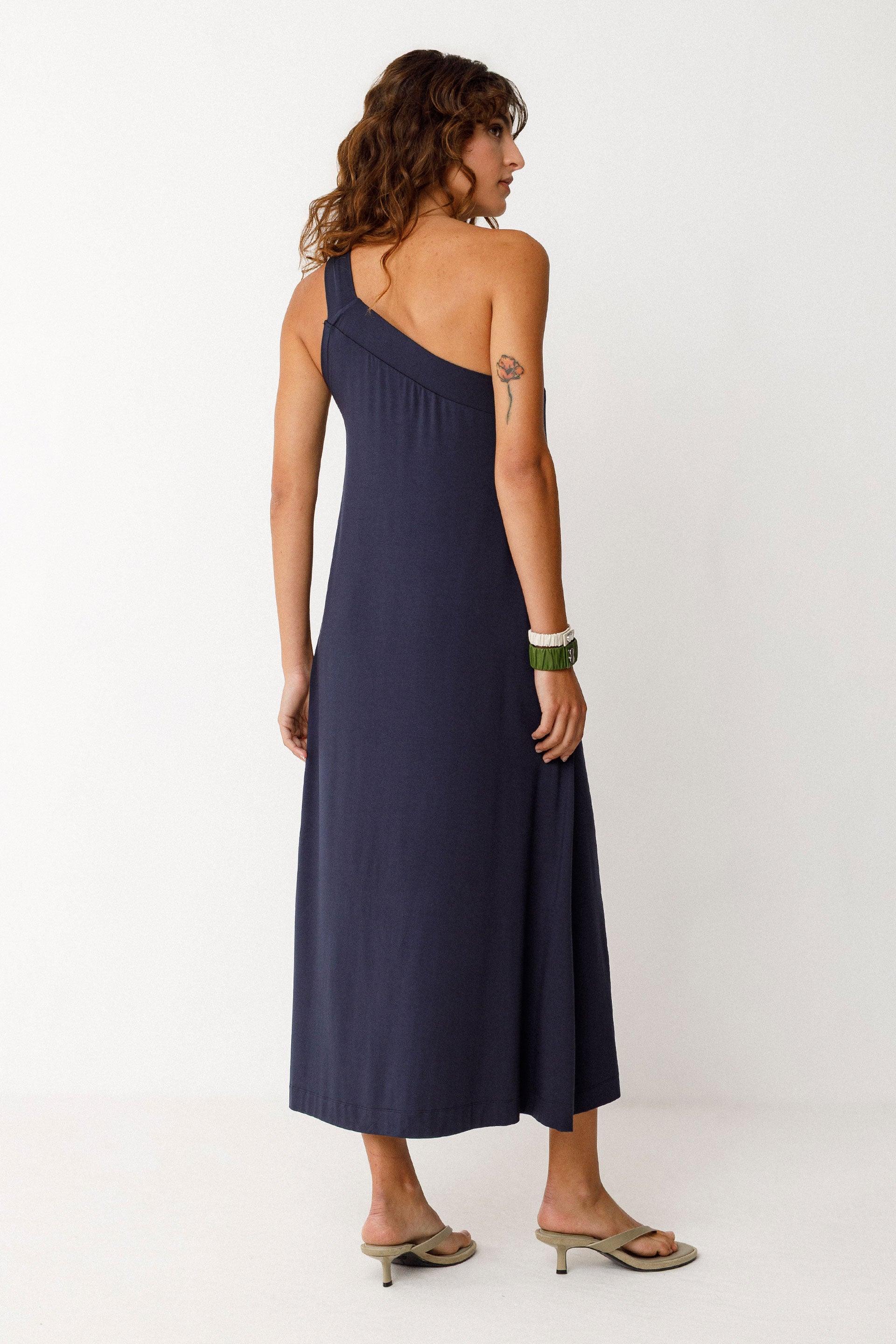 Woman wearing a navy blue tencel one-shoulder dress on a white background