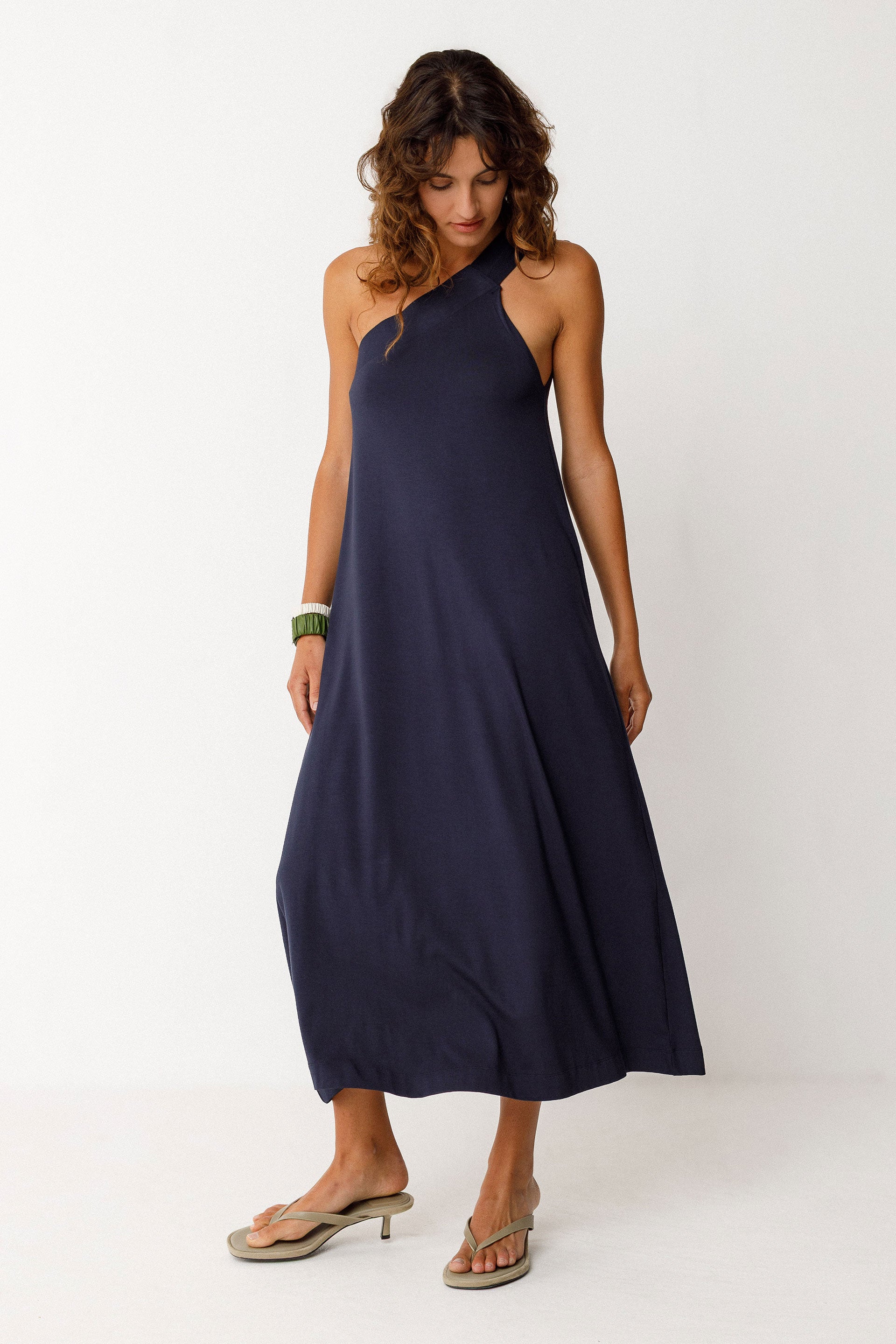Woman wearing a navy blue mid-length, A-line dress with asymmetrical shoulders on a white background