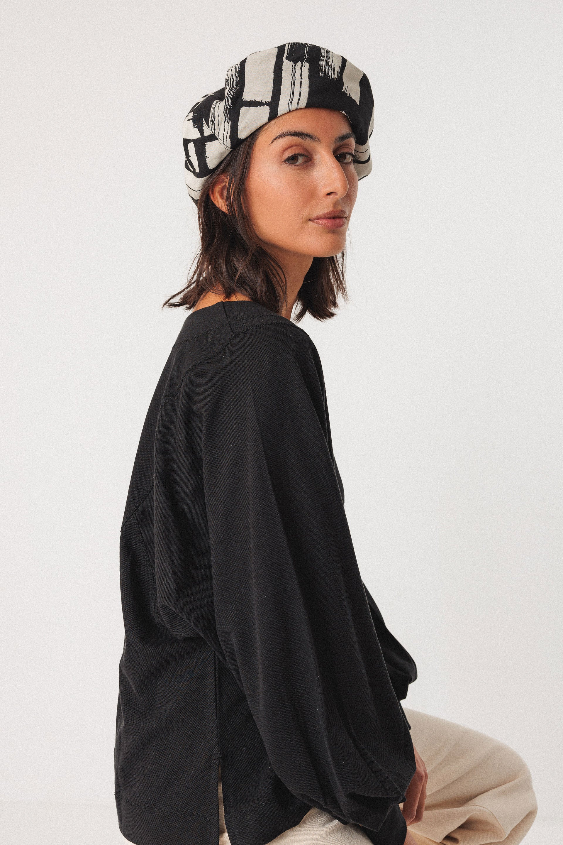 Woman wearing a black outfit and patterned organic cotton hat on a white background