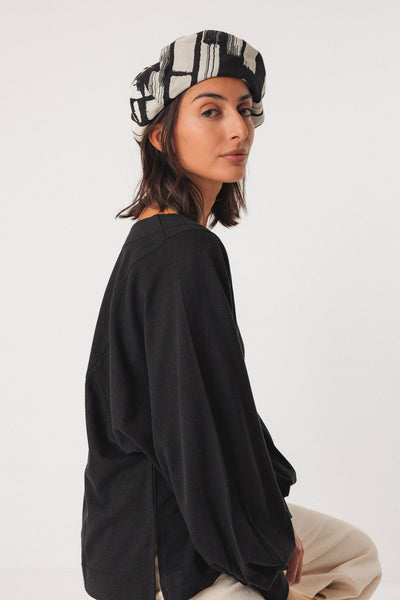Woman wearing a black outfit and patterned organic cotton hat on a white background