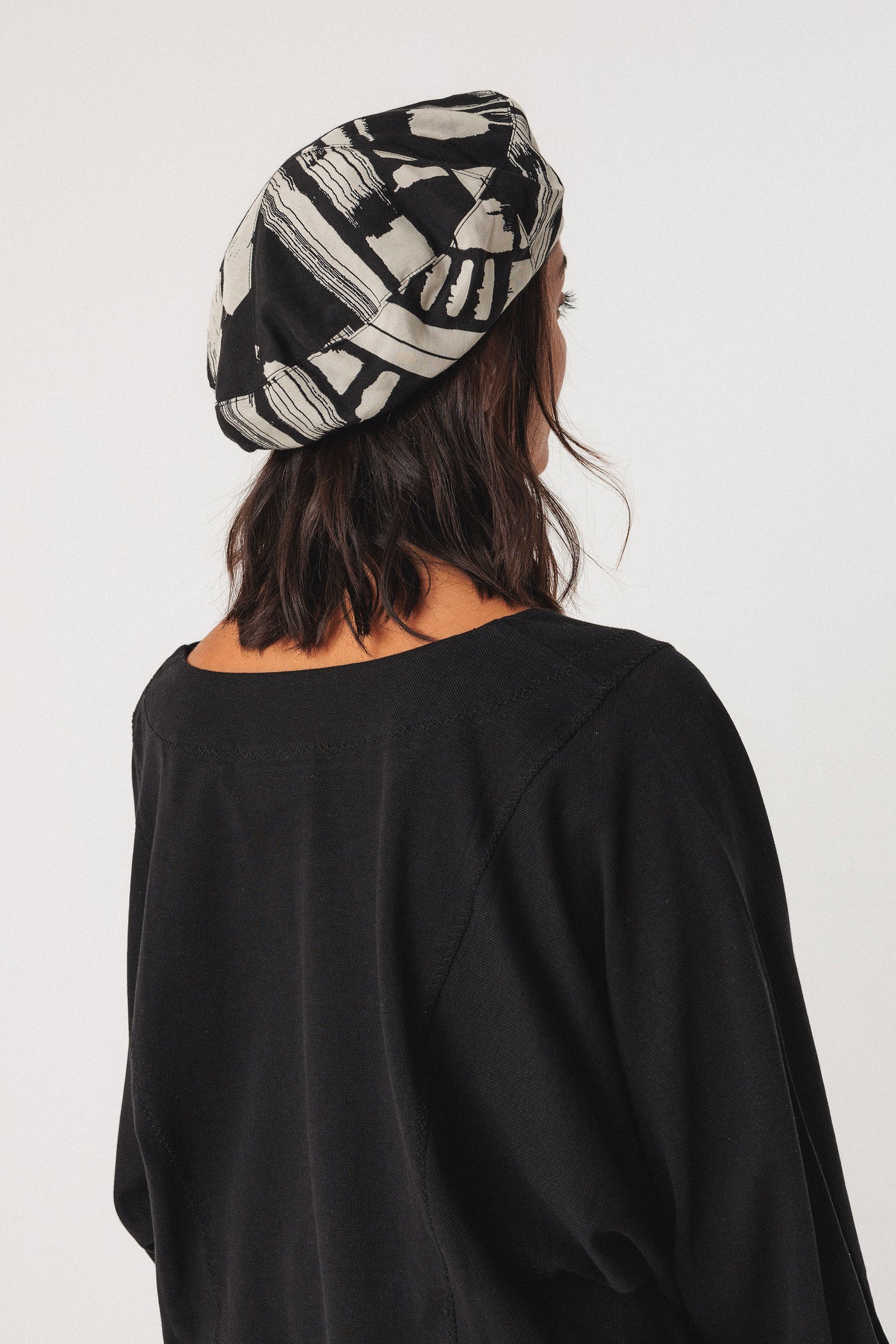 Person wearing a black and white patterned beret on a plain background