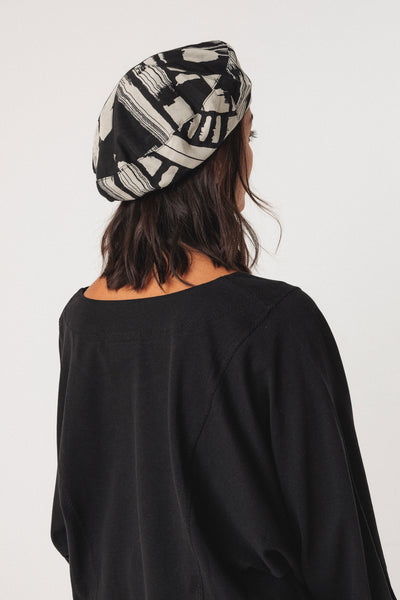 Person wearing a black and white patterned beret on a plain background