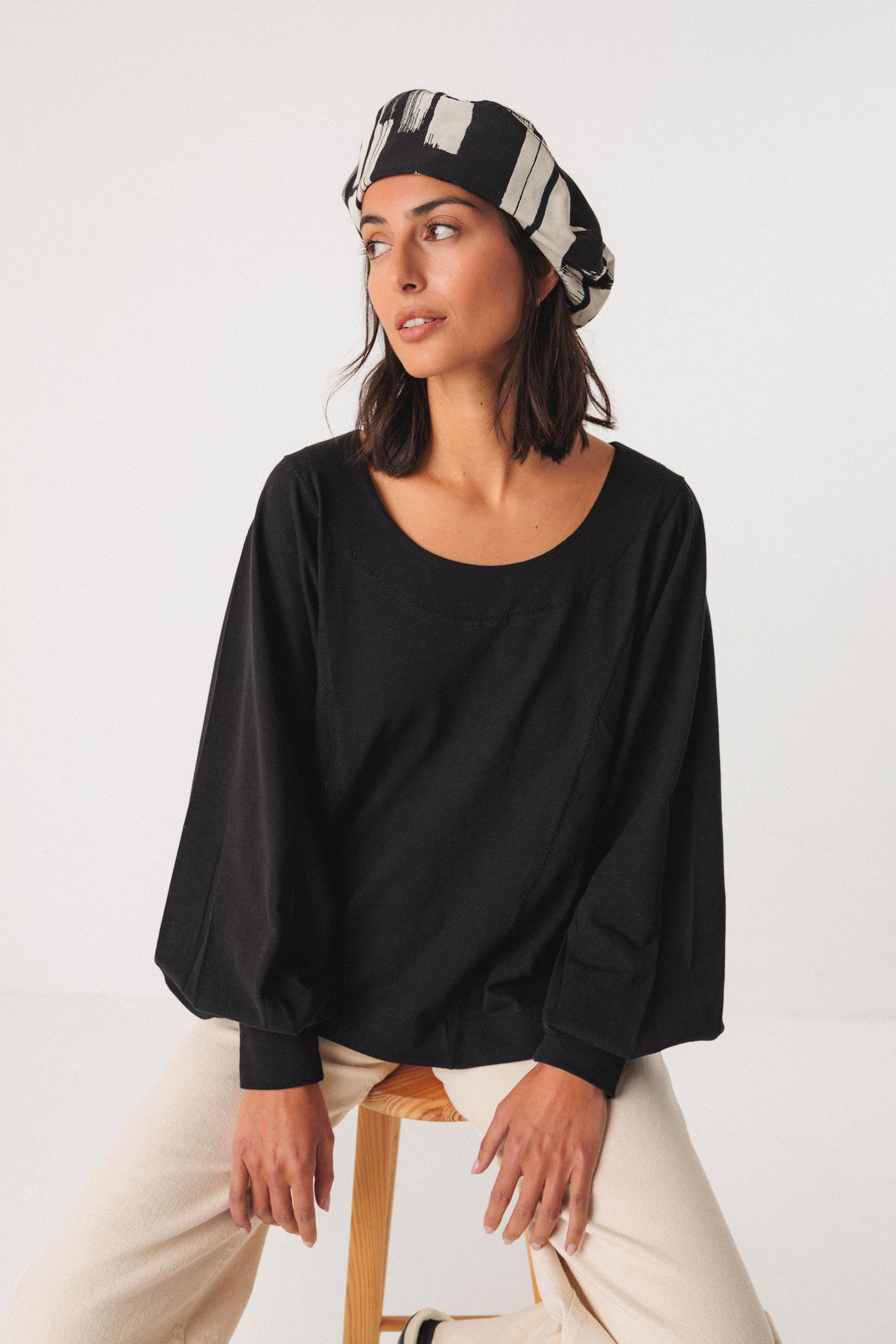 Woman wearing a black top and patterned organic cotton beret on a white background