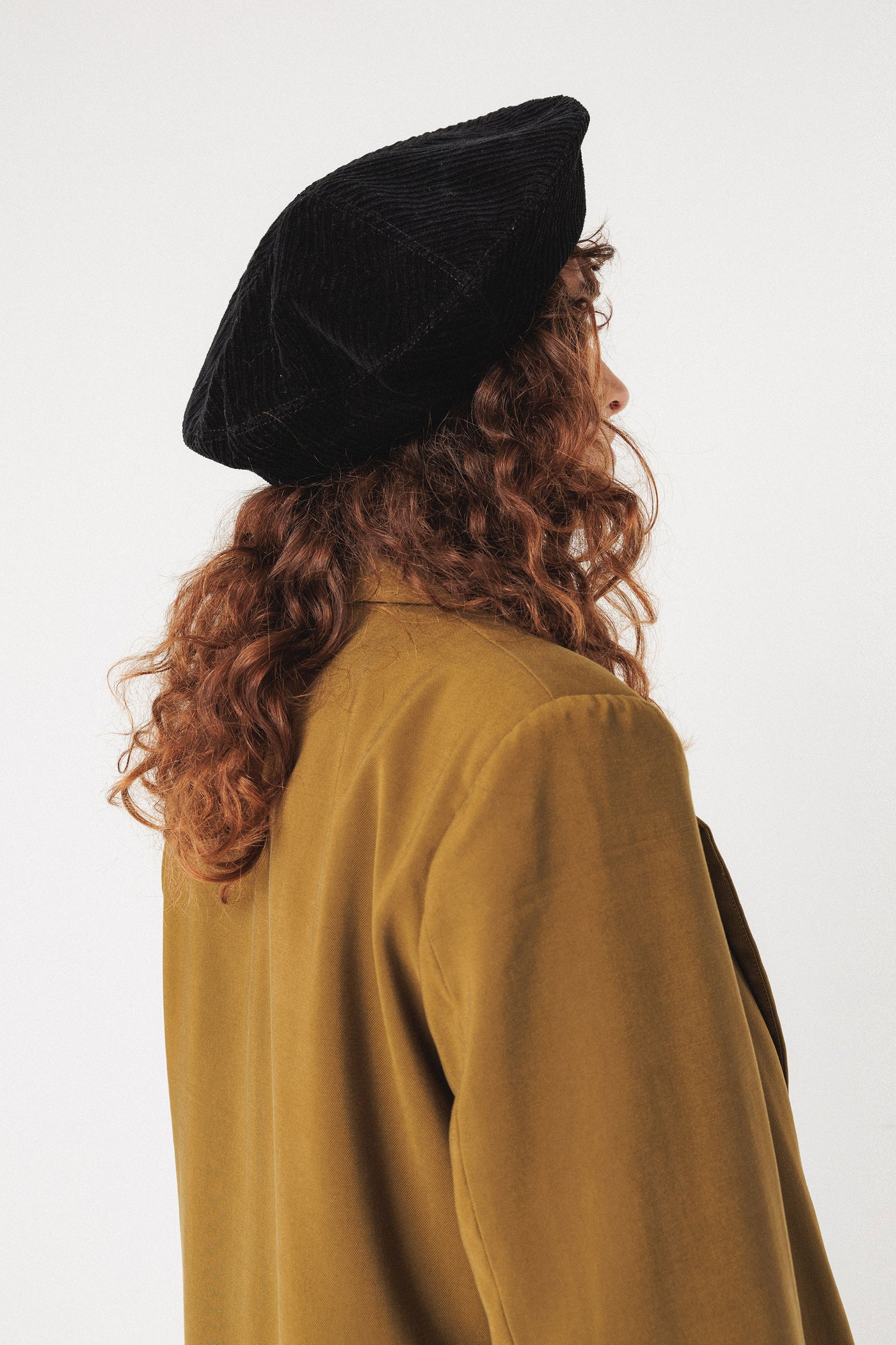 Person wearing a black organic cotton beret and mustard-colored coat on a white background
