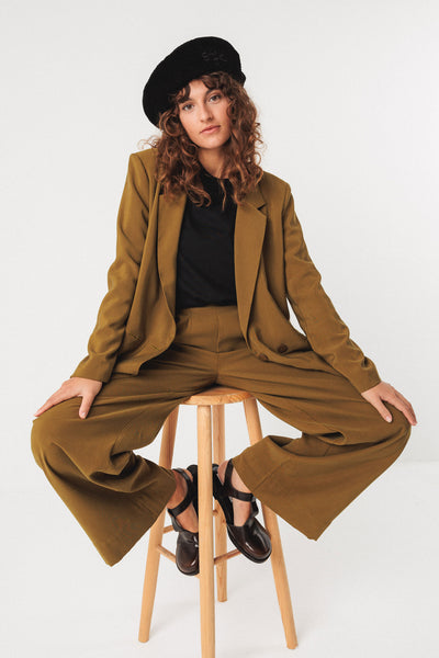 Woman in a brown suit sitting on a stool against a white background