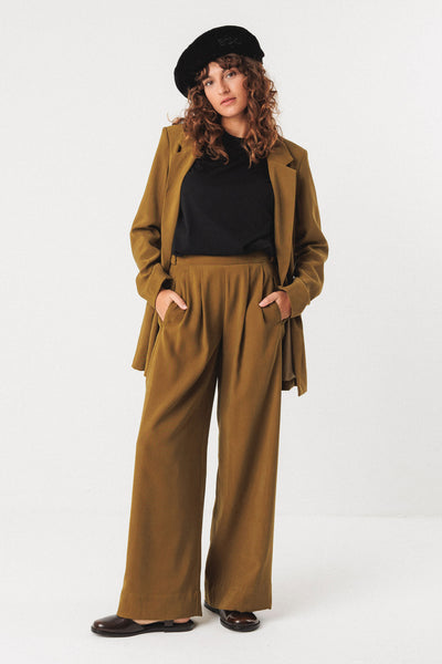 Woman wearing a brown coat and pants with a black organic cotton beret on a white background