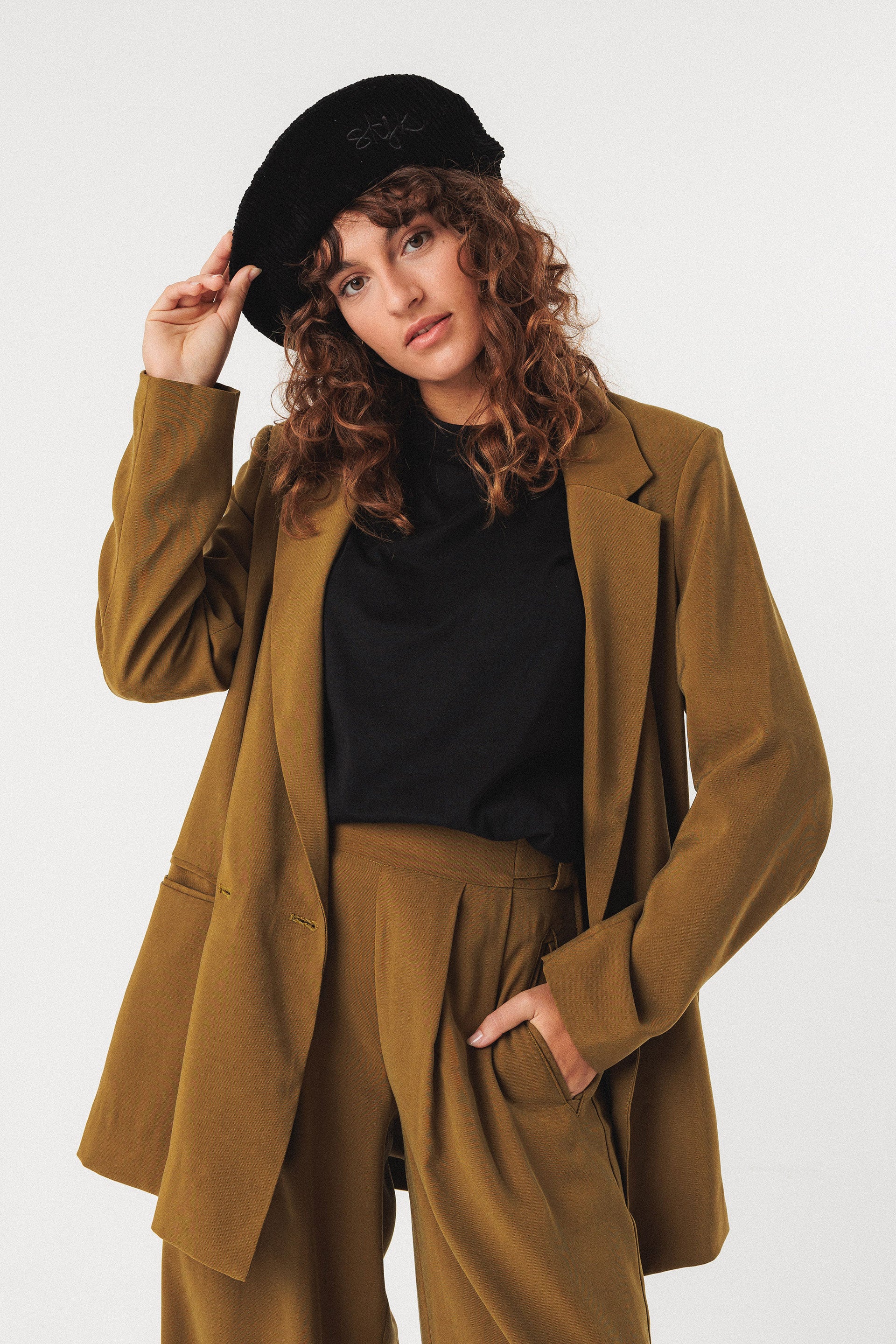 Woman wearing a brown suit and black organic cotton beret against a white background