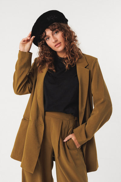 Woman wearing a brown suit and black organic cotton beret against a white background