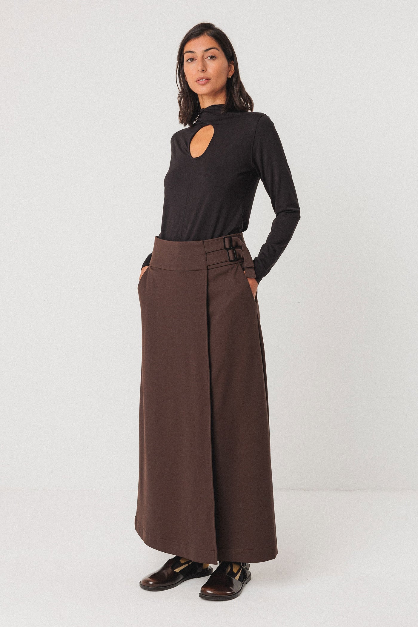 Woman wearing a black long-sleeve tencel top and brown wide-leg pants on a white background