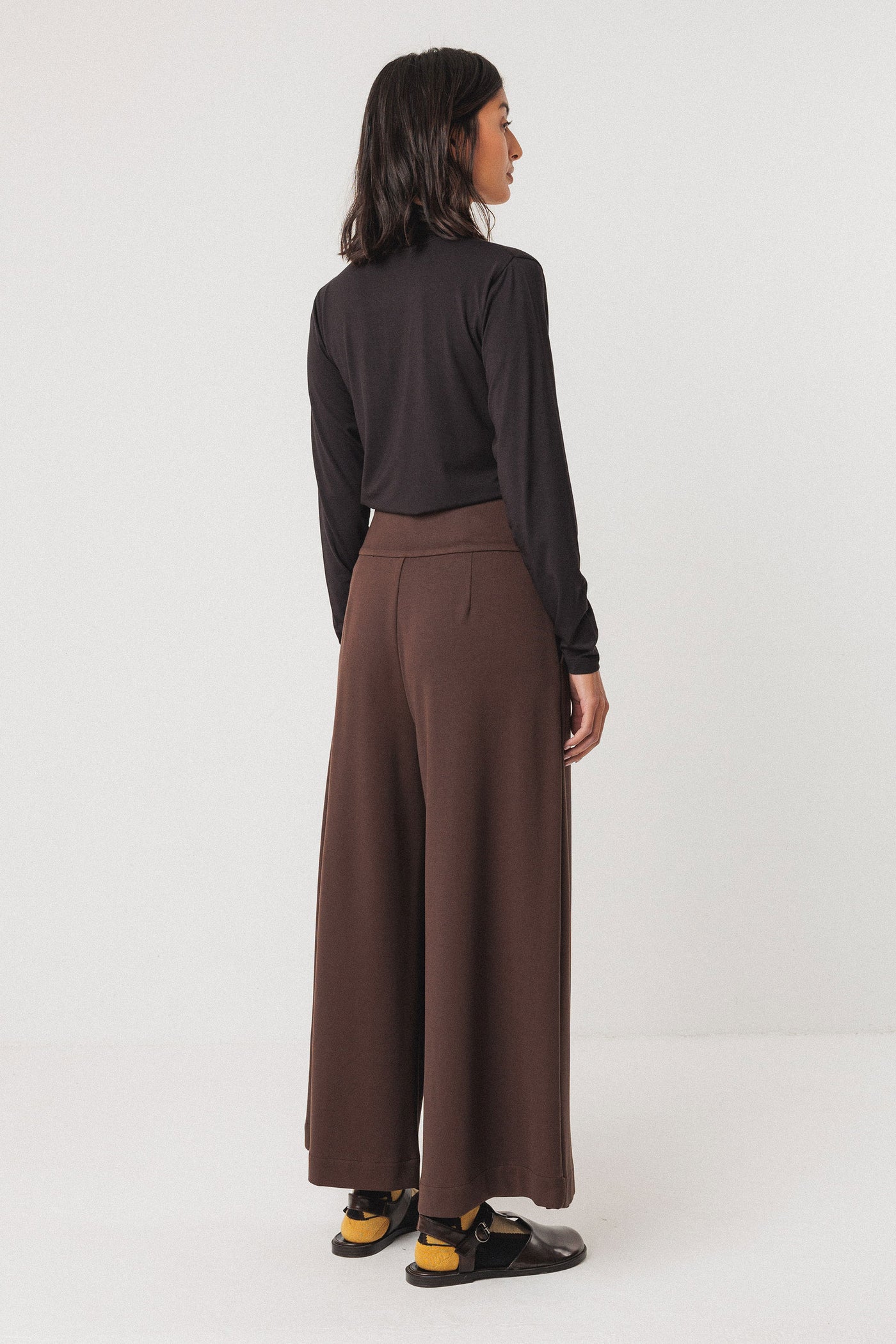 Person wearing a black tencel top and brown wide-leg pants on a white background