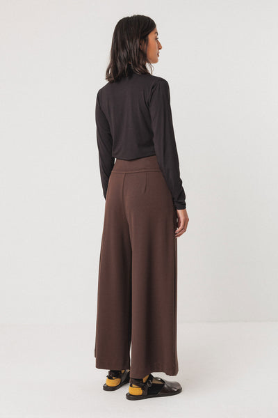 Person wearing a black tencel top and brown wide-leg pants on a white background