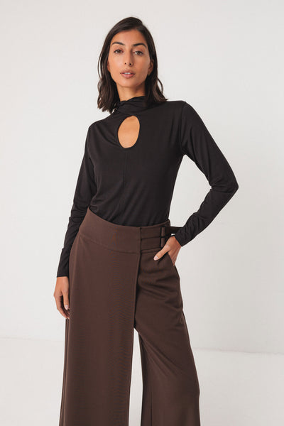 Woman wearing a black long-sleeve top with a cutout design and brown pants on a white background