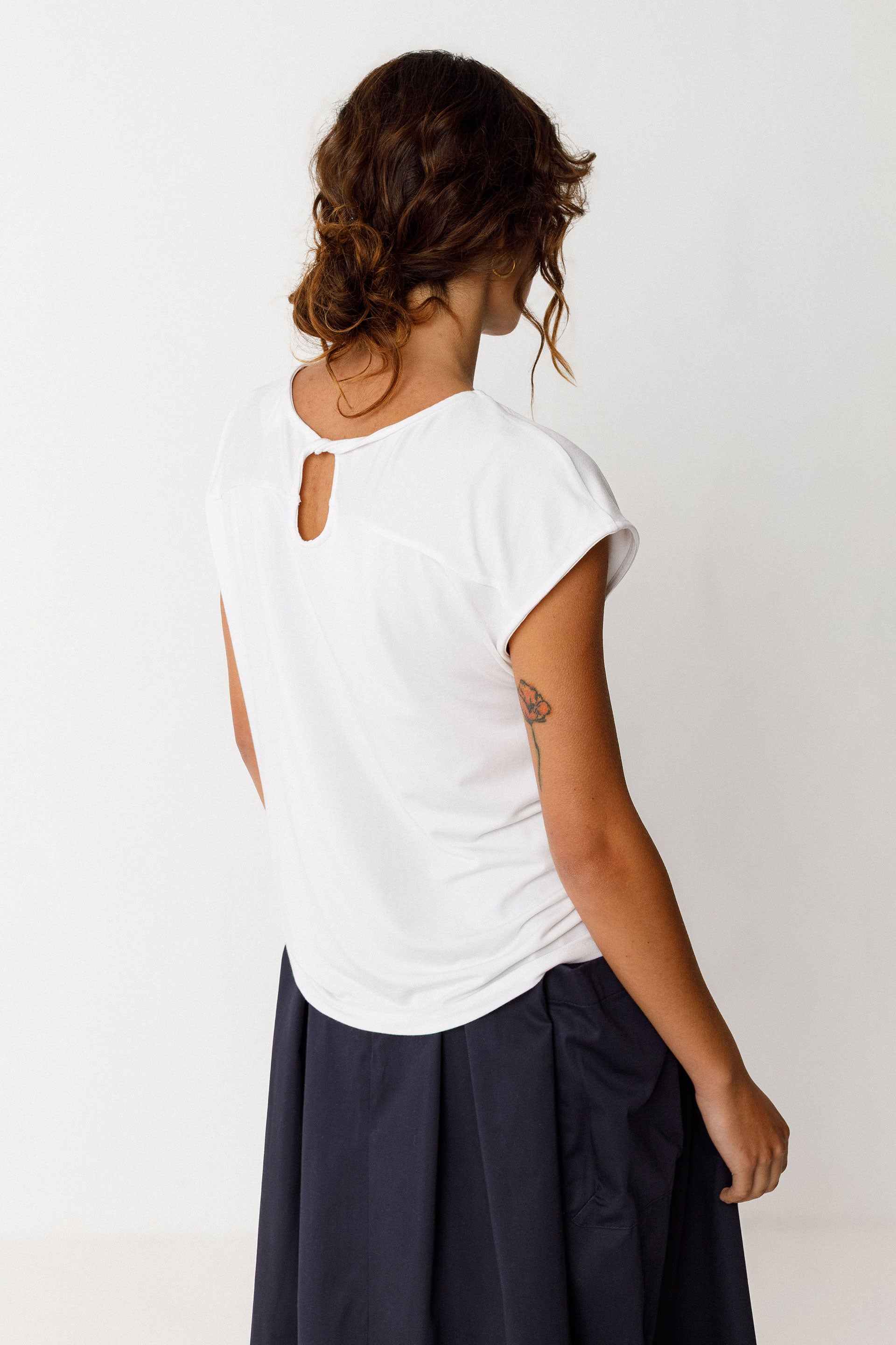 Woman wearing a white top with cut-out design on the back, standing against a plain background.