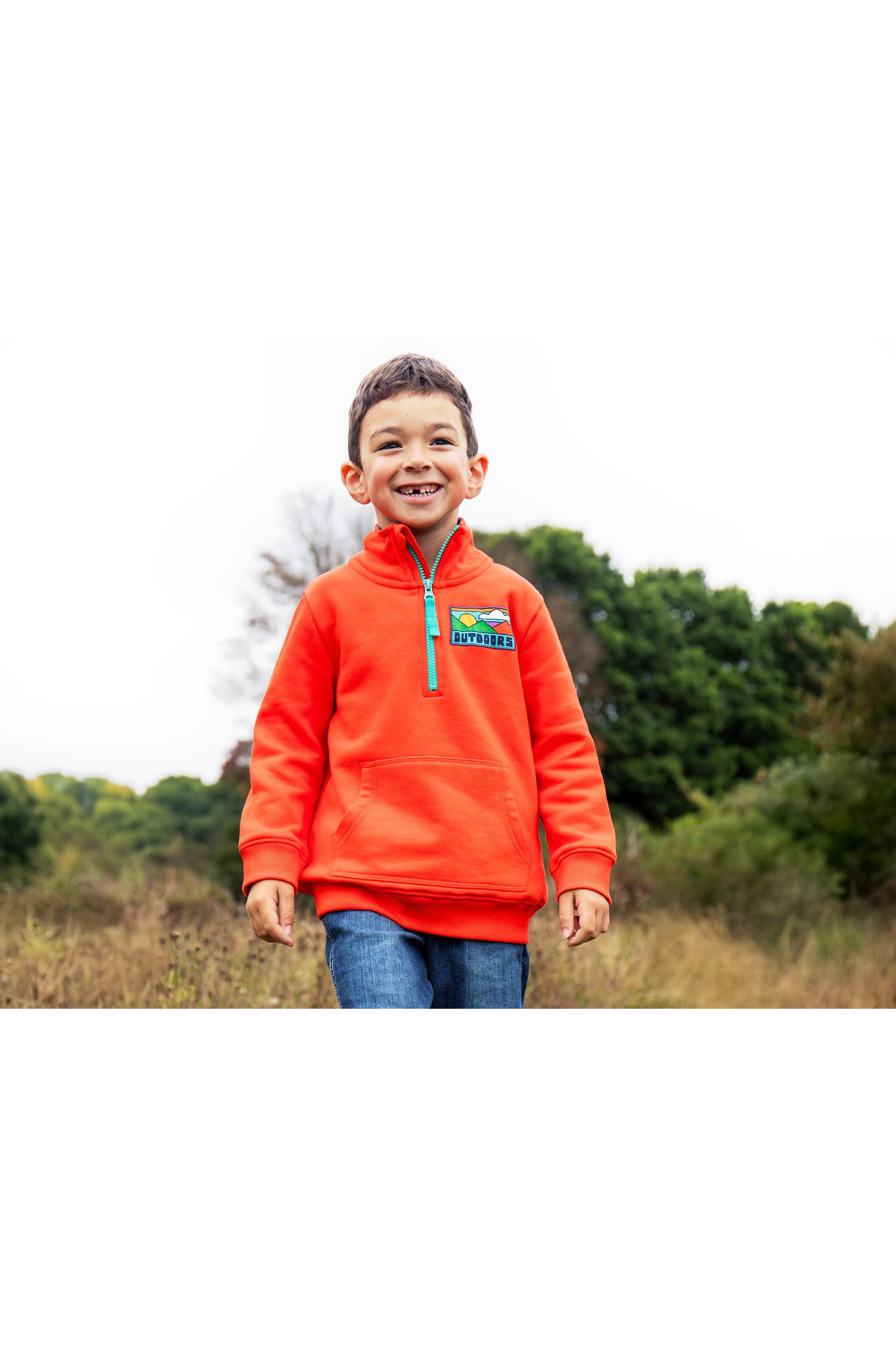 Child wearing an orange fleece jacket with a colorful logo in a natural setting