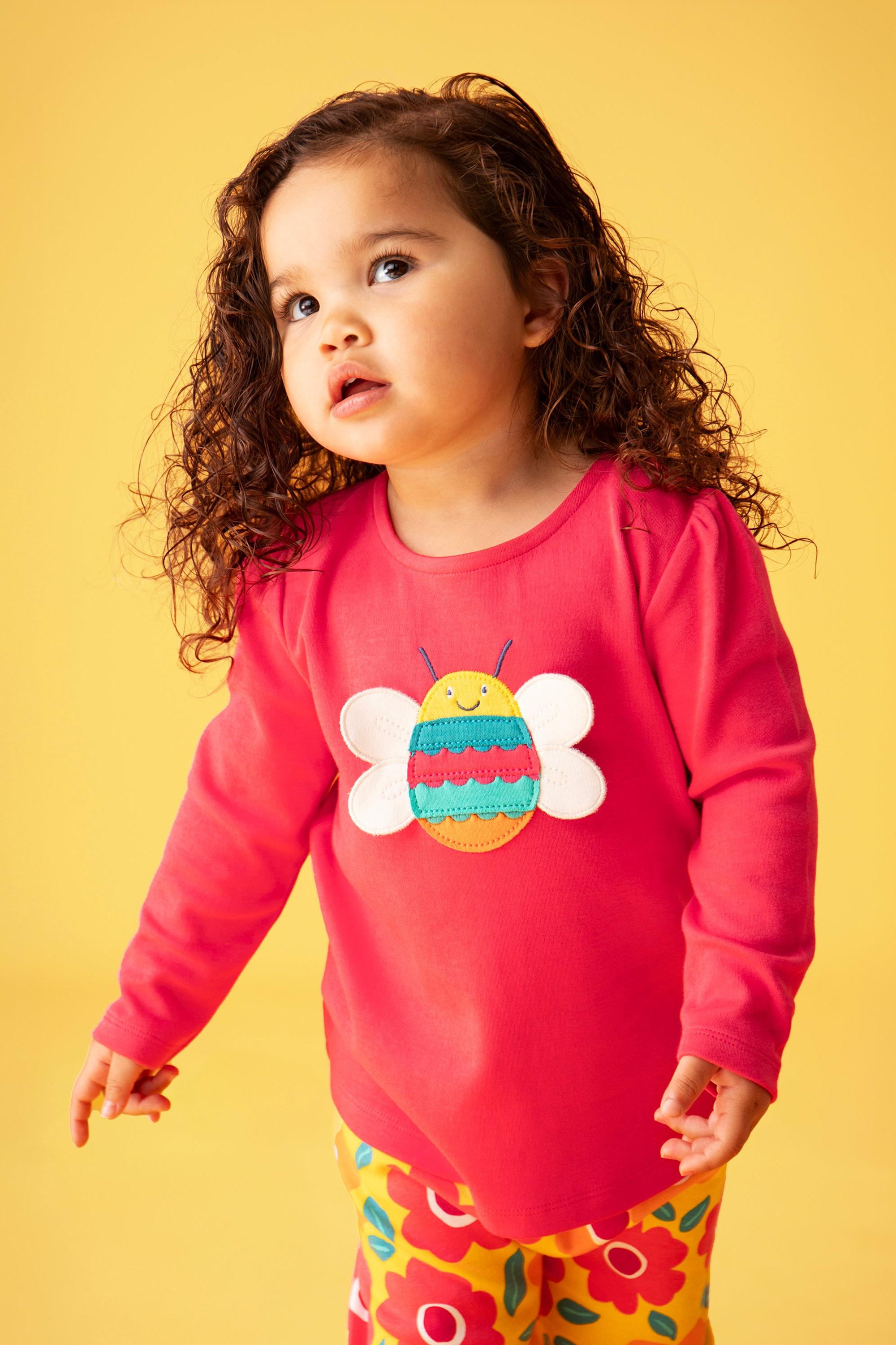 Child wearing a pink organic cotton shirt with a bee design on a yellow background