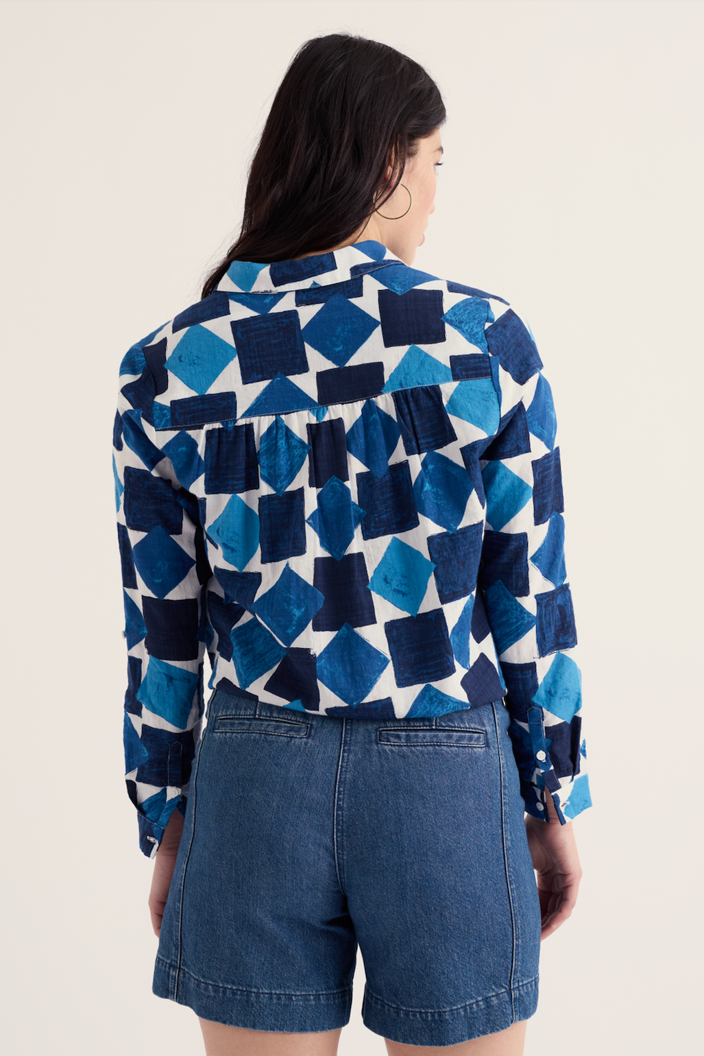 Person wearing a blue and white geometric patterned shirt with denim shorts on a beige background