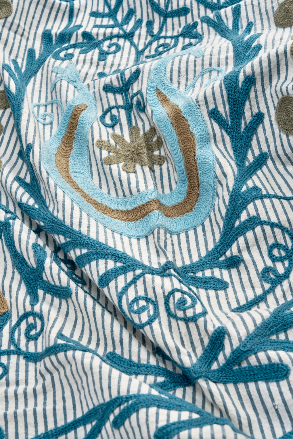 Intricate blue and tan floral embroidery patterns stitched onto a blue and white striped cotton fabric.